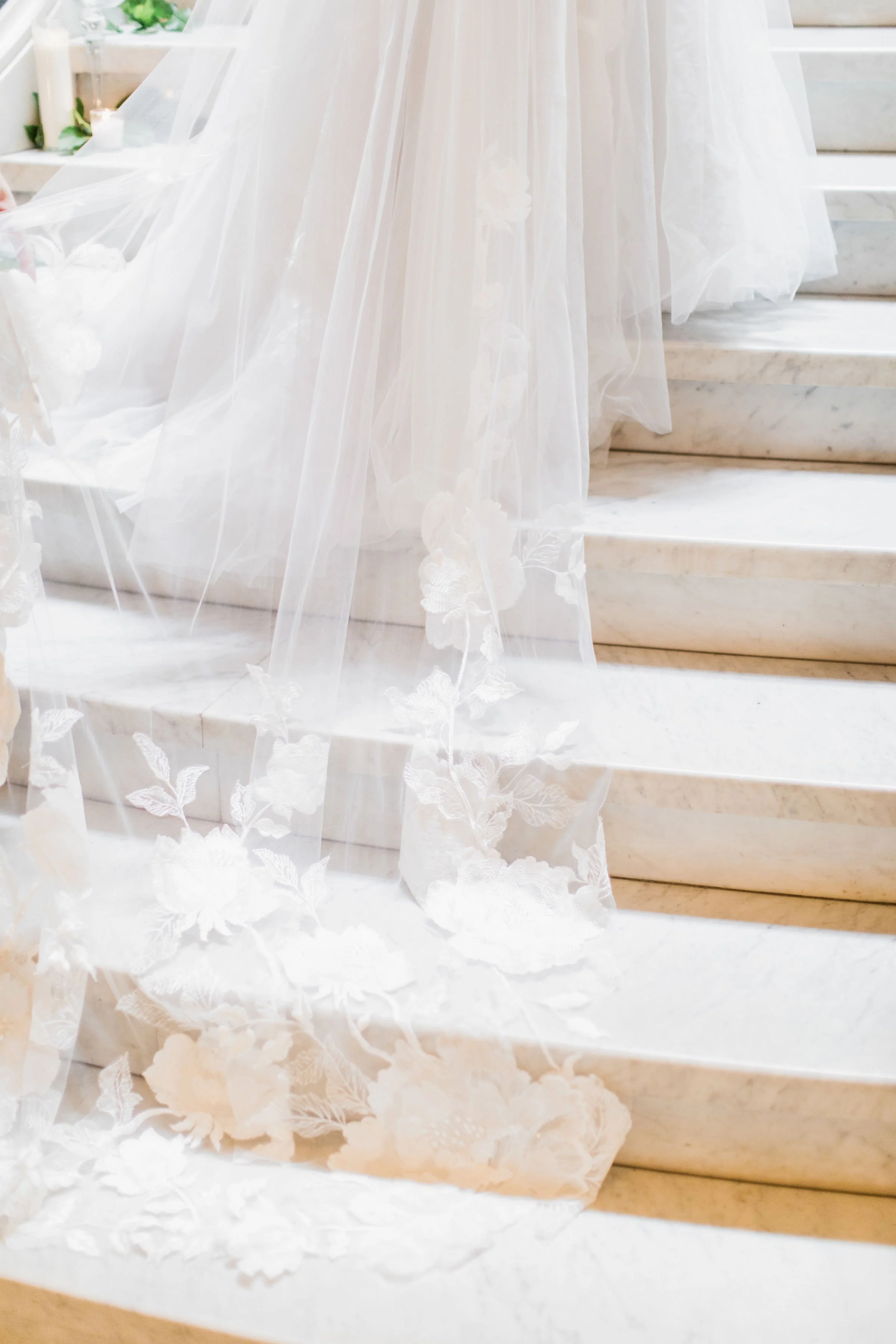 Close-up of a wedding dress with lace and tulle train on marble stairs.