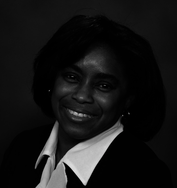 Black and white portrait of a woman with short dark hair, smiling, wearing a white collared shirt and dark blazer, with hoop earrings.