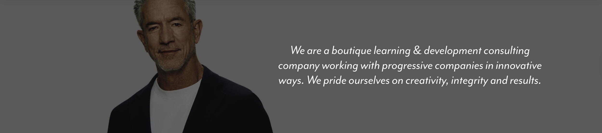 A middle-aged man with gray hair and a beard, wearing a dark blazer and a white t-shirt, standing against a gray background with a quote about a learning and development consulting company.