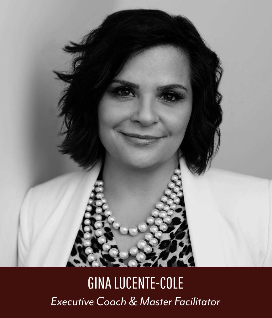 Black and white portrait of Gina Lucente-Cole, an executive coach and master facilitator, smiling with short wavy hair, wearing pearl necklaces and a leopard print top with a white blazer, against a plain background.