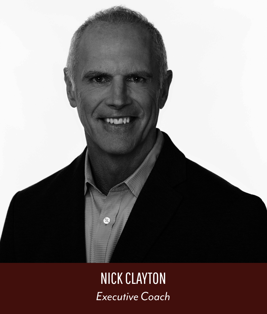 Black and white professional headshot of Nick Clayton, an executive coach, smiling, with a light-colored shirt and dark blazer, against a plain background.
