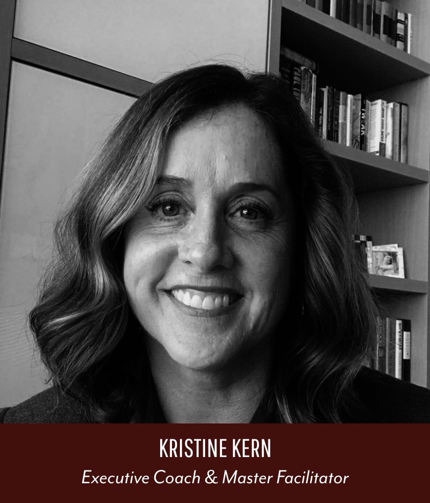 Black and white portrait of Kristine Kern smiling, with wavy hair, in front of a bookshelf with books and framed photo.