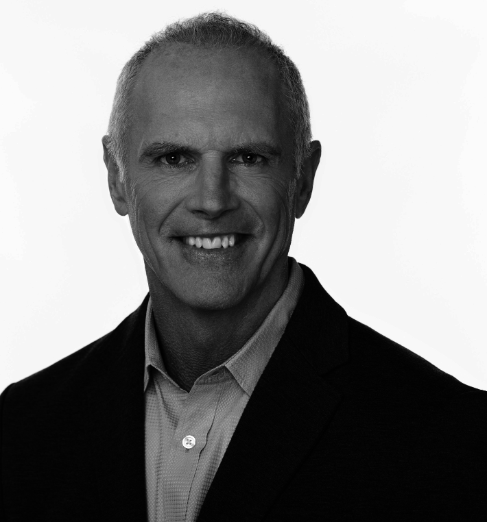 Black and white professional headshot of a smiling middle-aged man wearing a suit jacket and dress shirt.
