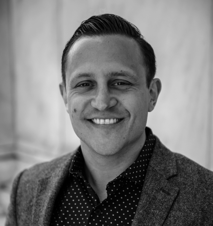 Black and white portrait of a smiling man in a polka dot shirt and blazer.