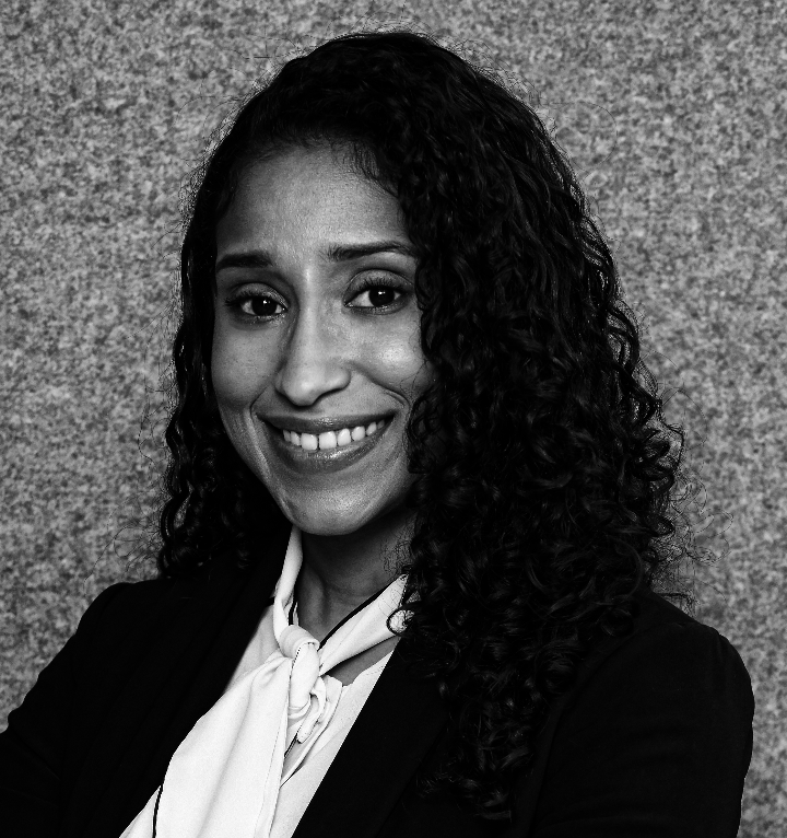 A professional woman with curly hair smiling in front of a textured wall.