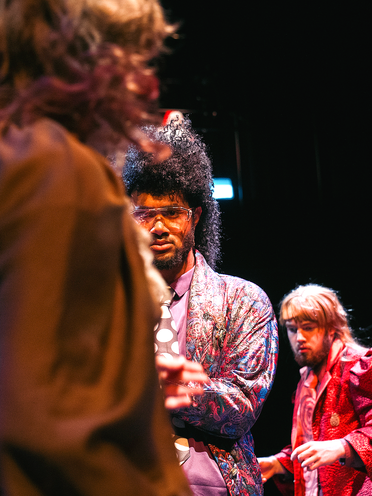 Three people in colorful, patterned suits in a dimly lit environment, with one person's face in focus and two others partially visible.
