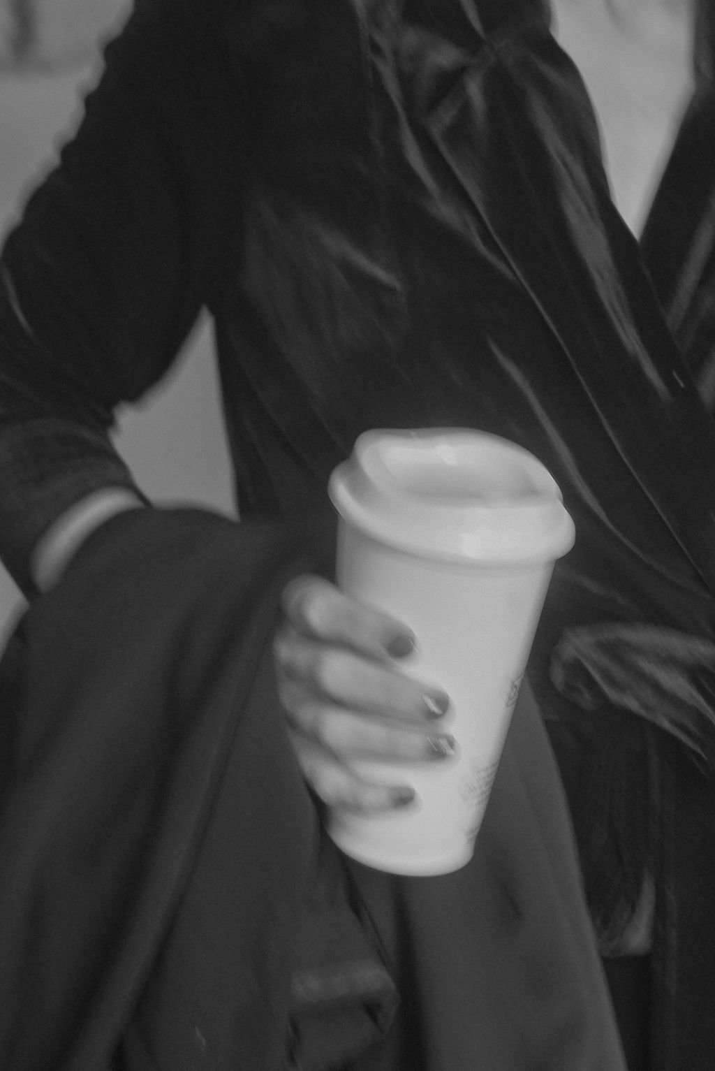 Person in dark clothing holding a disposable coffee cup.