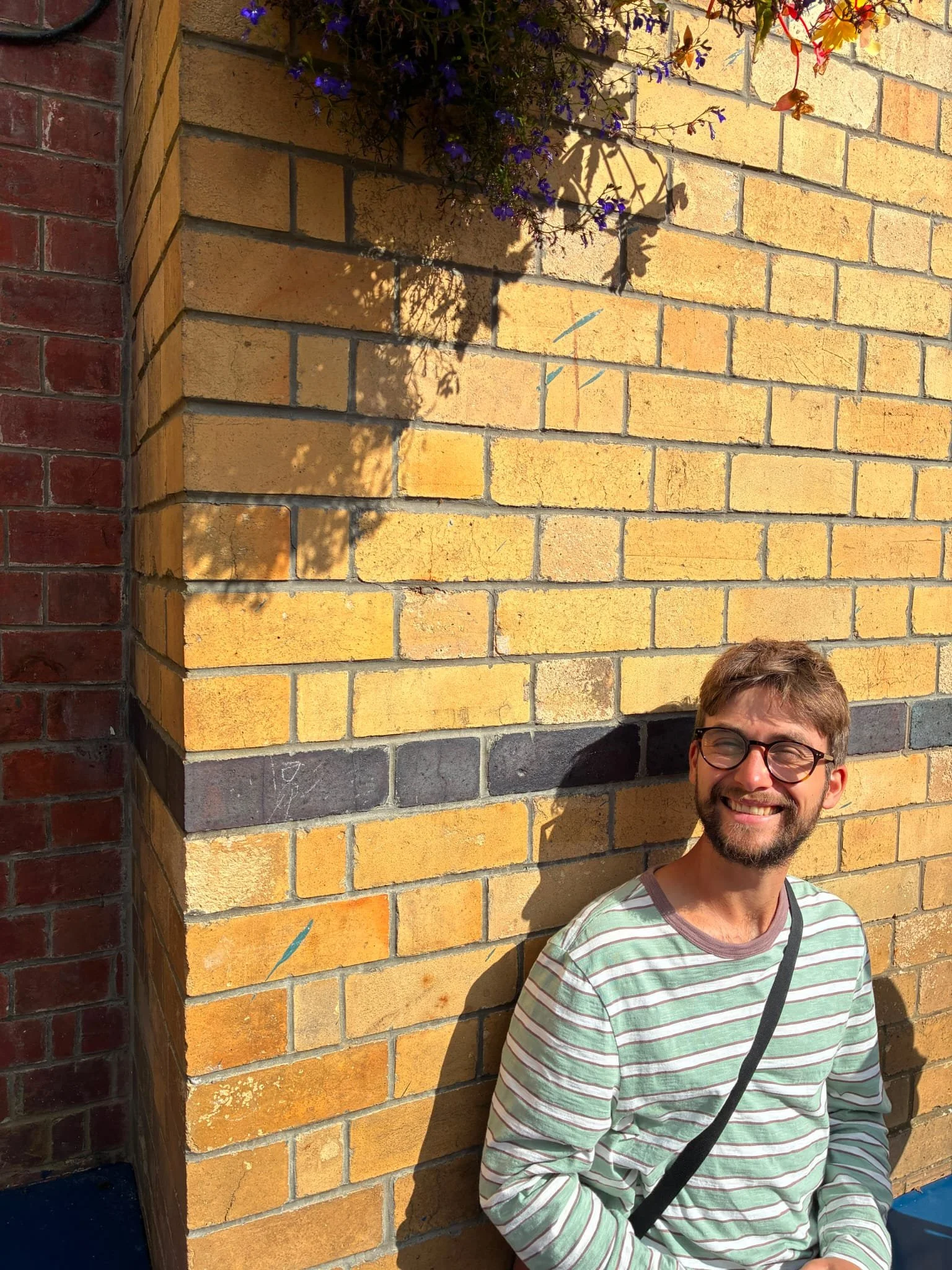 Mr Noakes smiling in the sun against a brick wall and hanging flowers