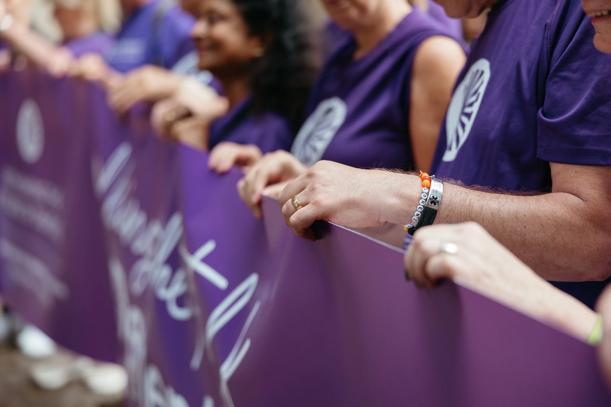 People holding a purple banner at a rally or event, wearing purple shirts.
