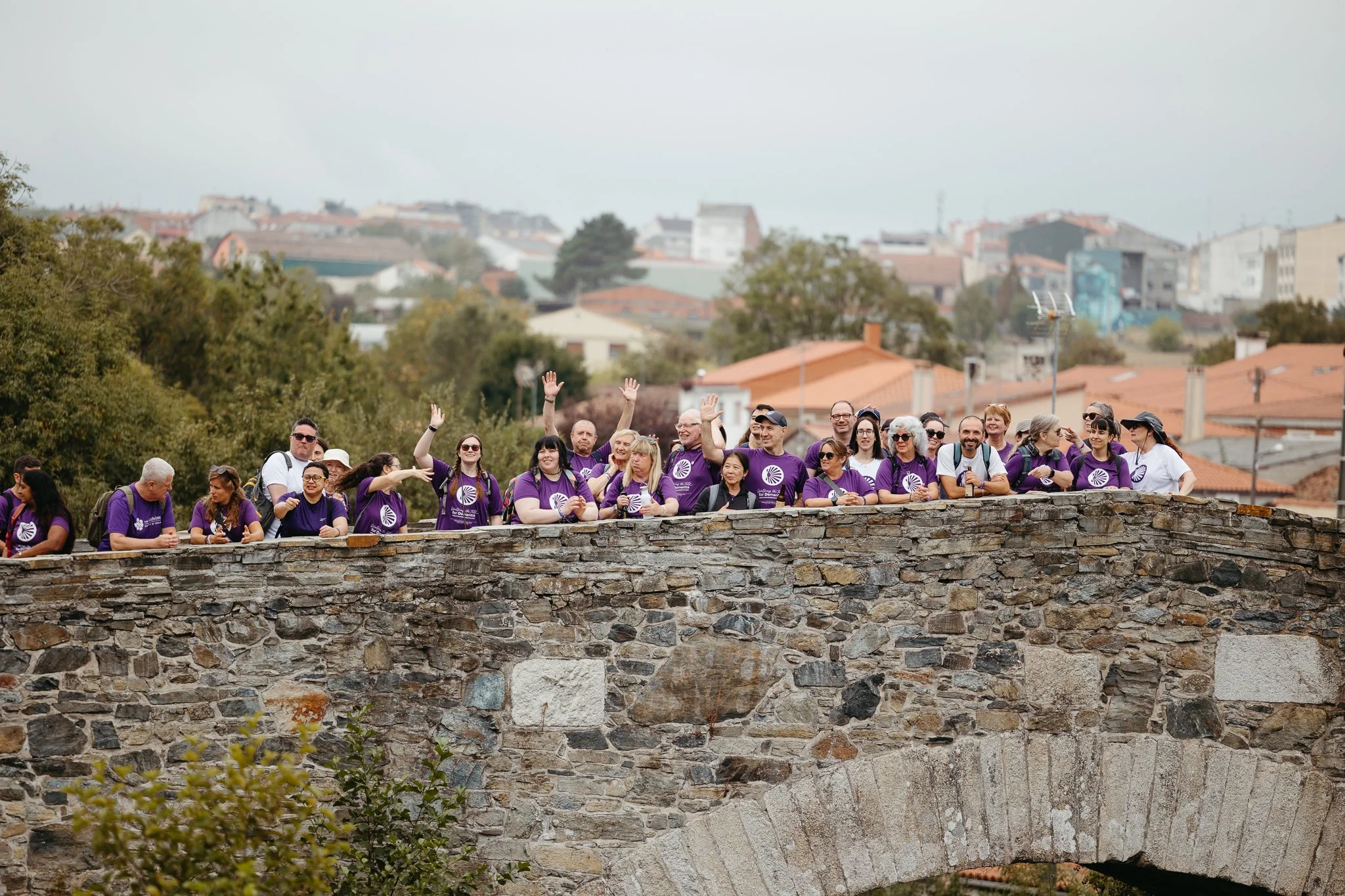 Group of people wearing purple shirts walking on a stone bridge in an urban area.