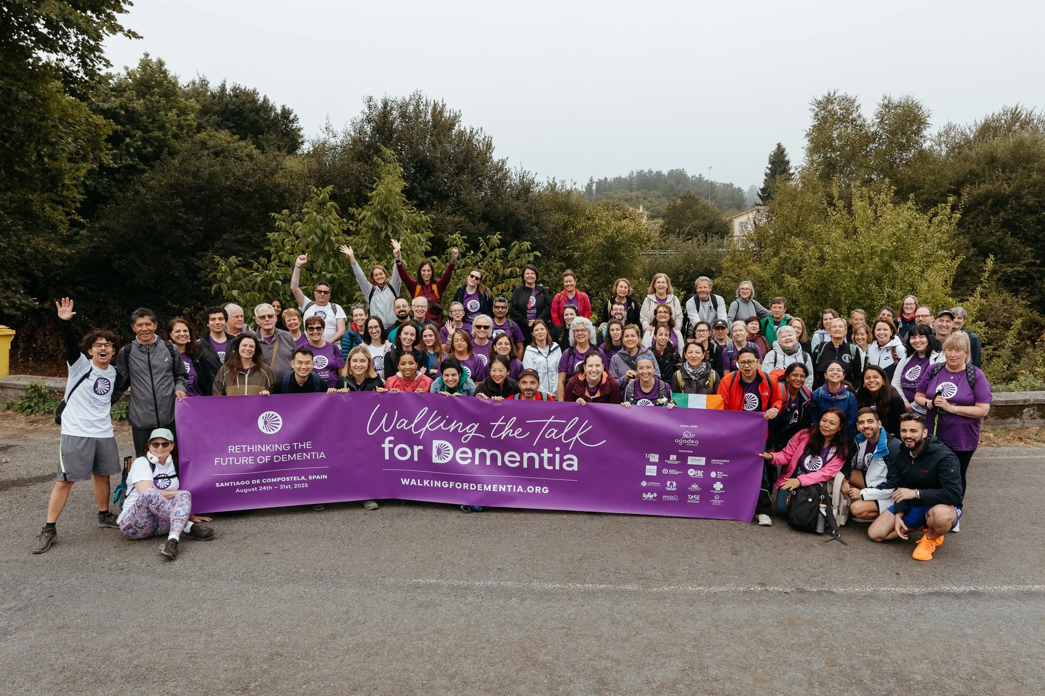 A large group of people holding a purple banner with the text 'Walking the Talk for Dementia' and 'Rethinking the Future of Dementia' during an outdoor event in Santiago de Compostela, Spain, in 2023. The group includes men and women of various ages,