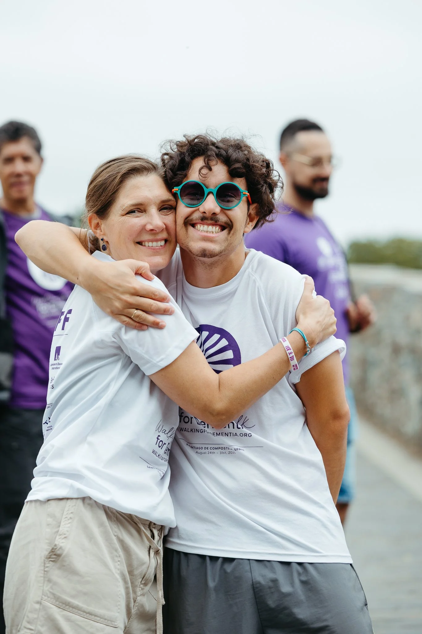 Two people smiling and hugging at a walking event, with others in the background.