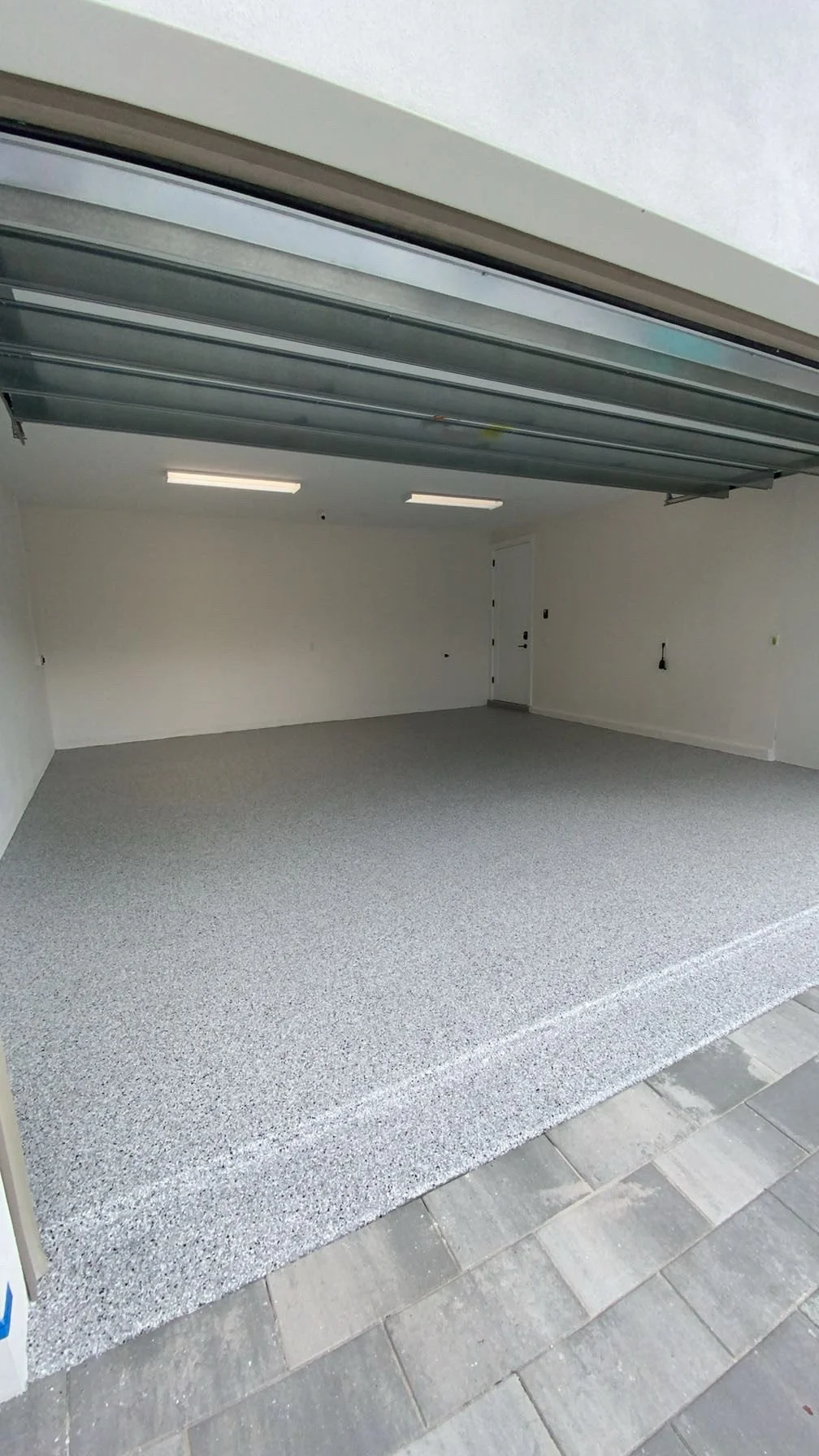 Empty garage with open door, gray speckled epoxy floor, white walls, and ceiling lights.