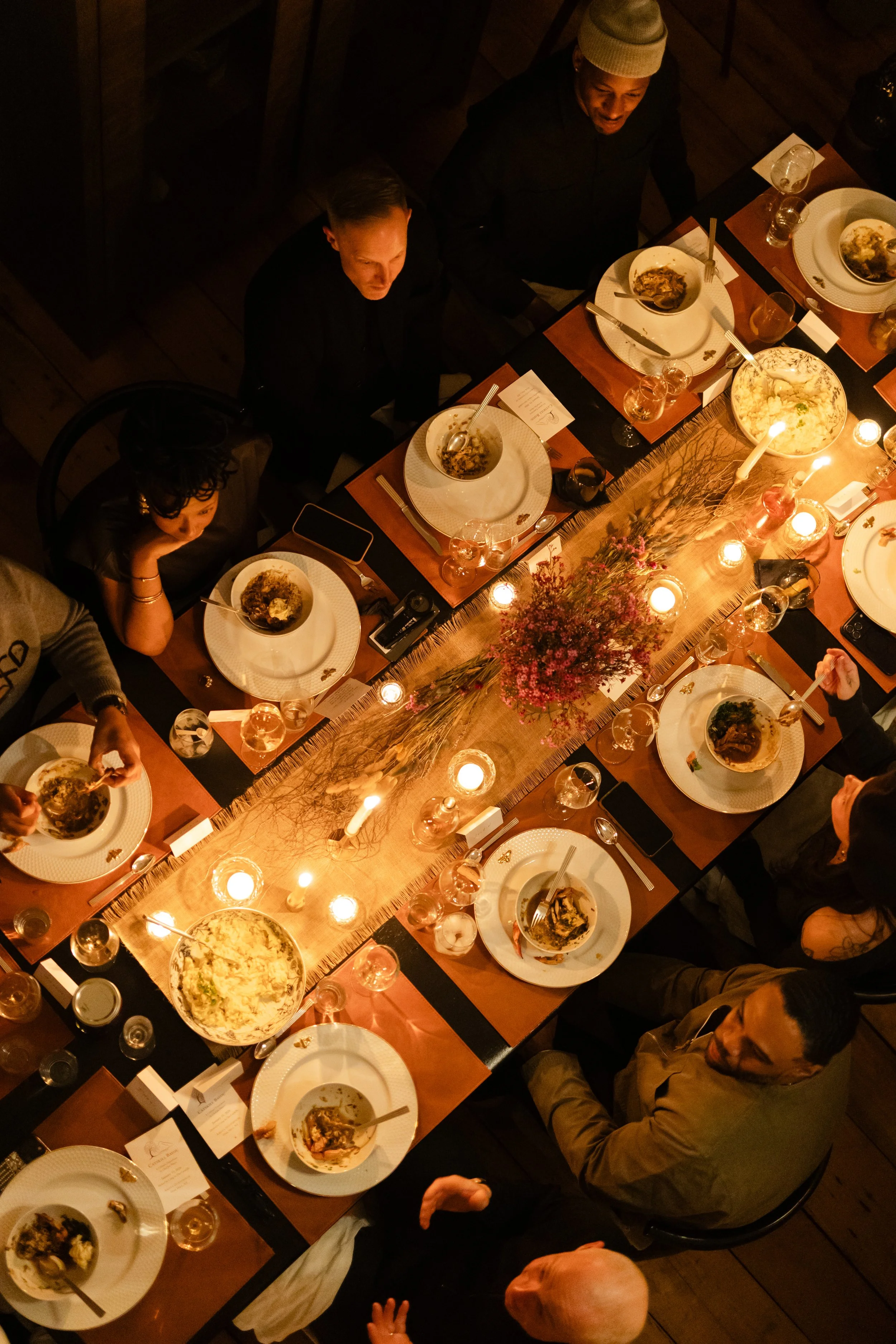 A restaurant table with a plate of gourmet food, including greens and sauce, and glassware, including wine glasses and a bottle of water, in a dimly lit setting with candles in the background.