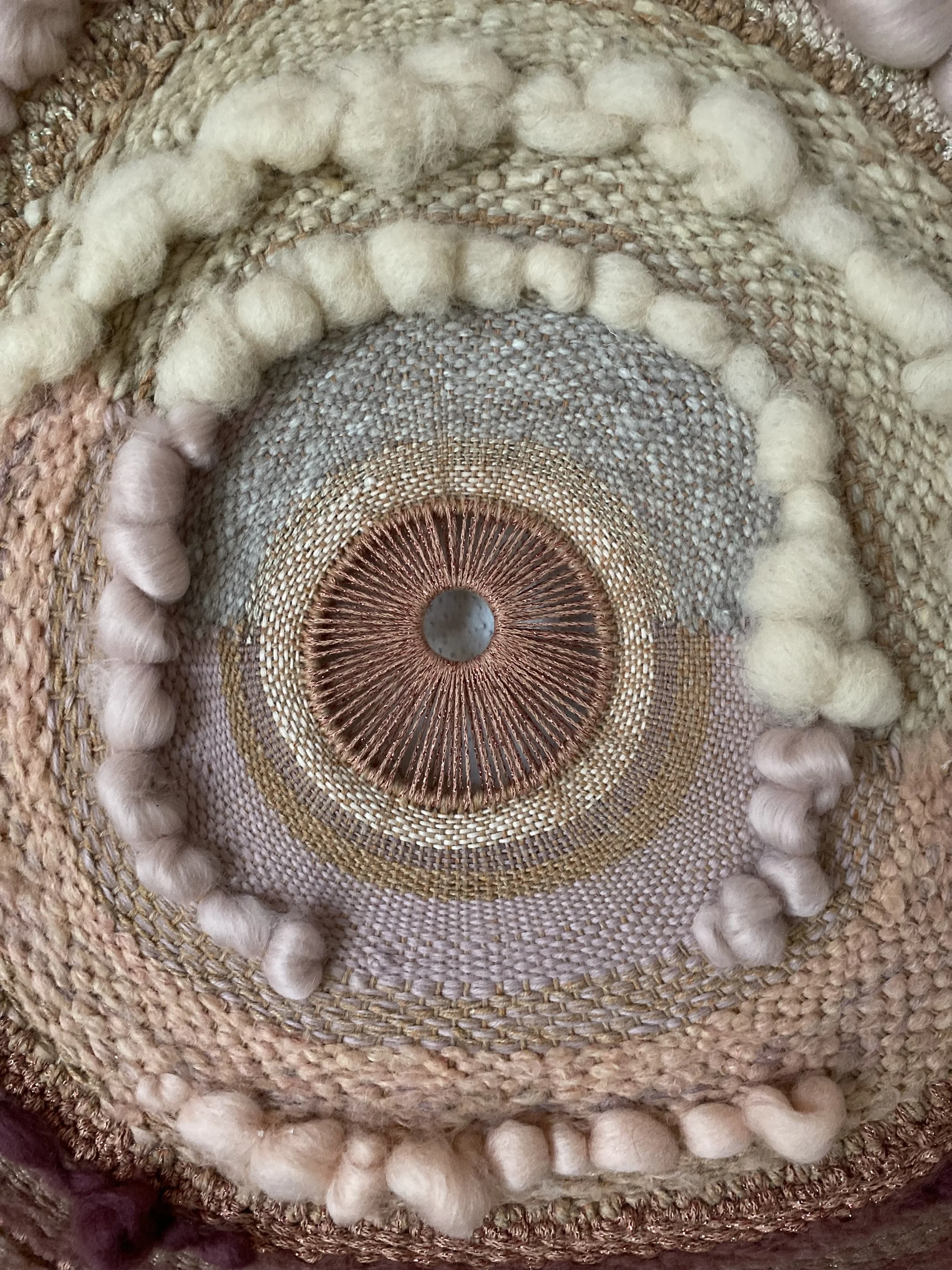 Close-up of a woven, circular textile with various textured layers and a central metal ring.