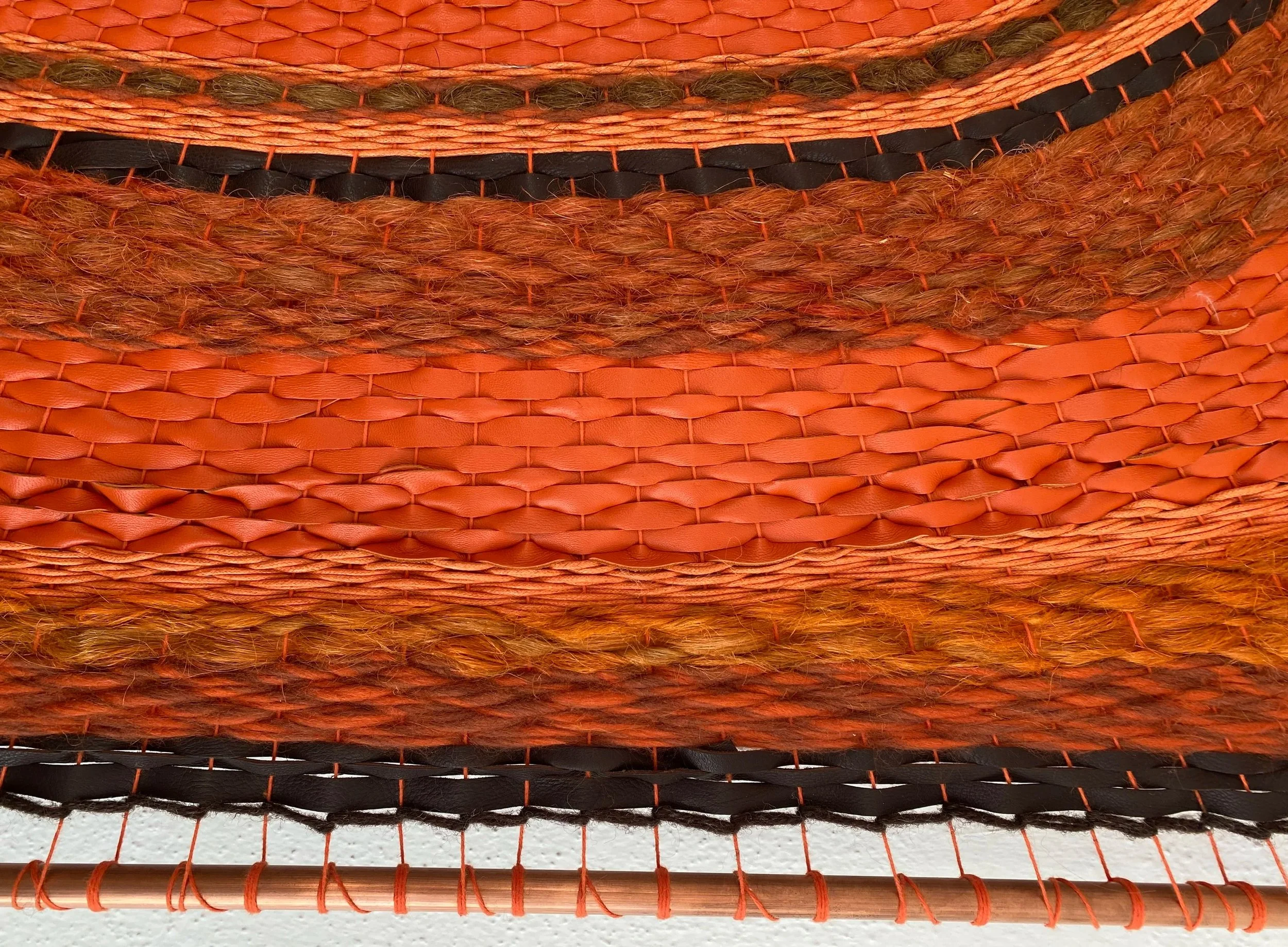 Close-up of various intertwined and textured orange and black artificial fibers, possibly a woven decorative item or material on a white surface.