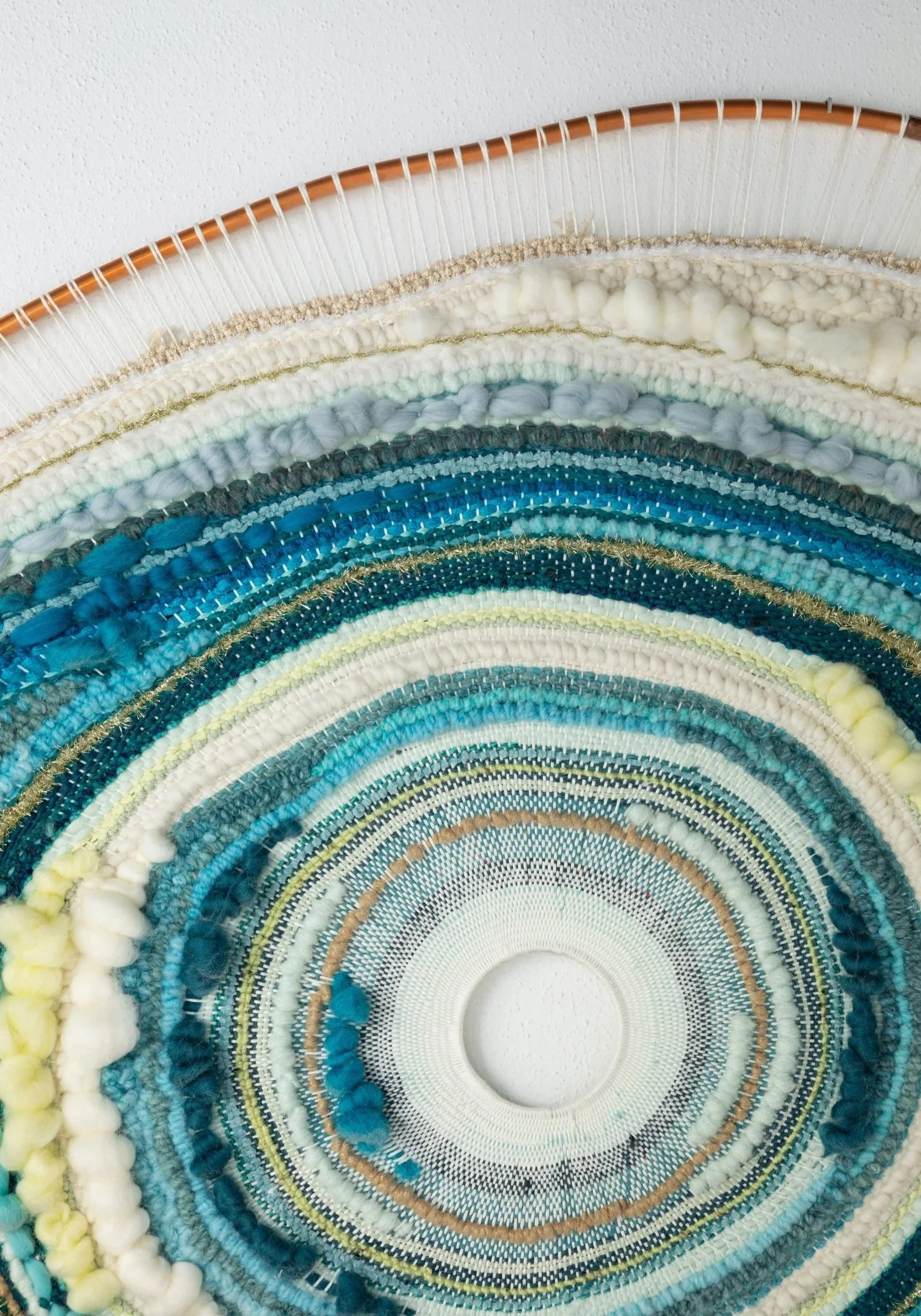 Close-up of a circular woven wall hanging with various shades of blue, white, yellow, and gold yarns.