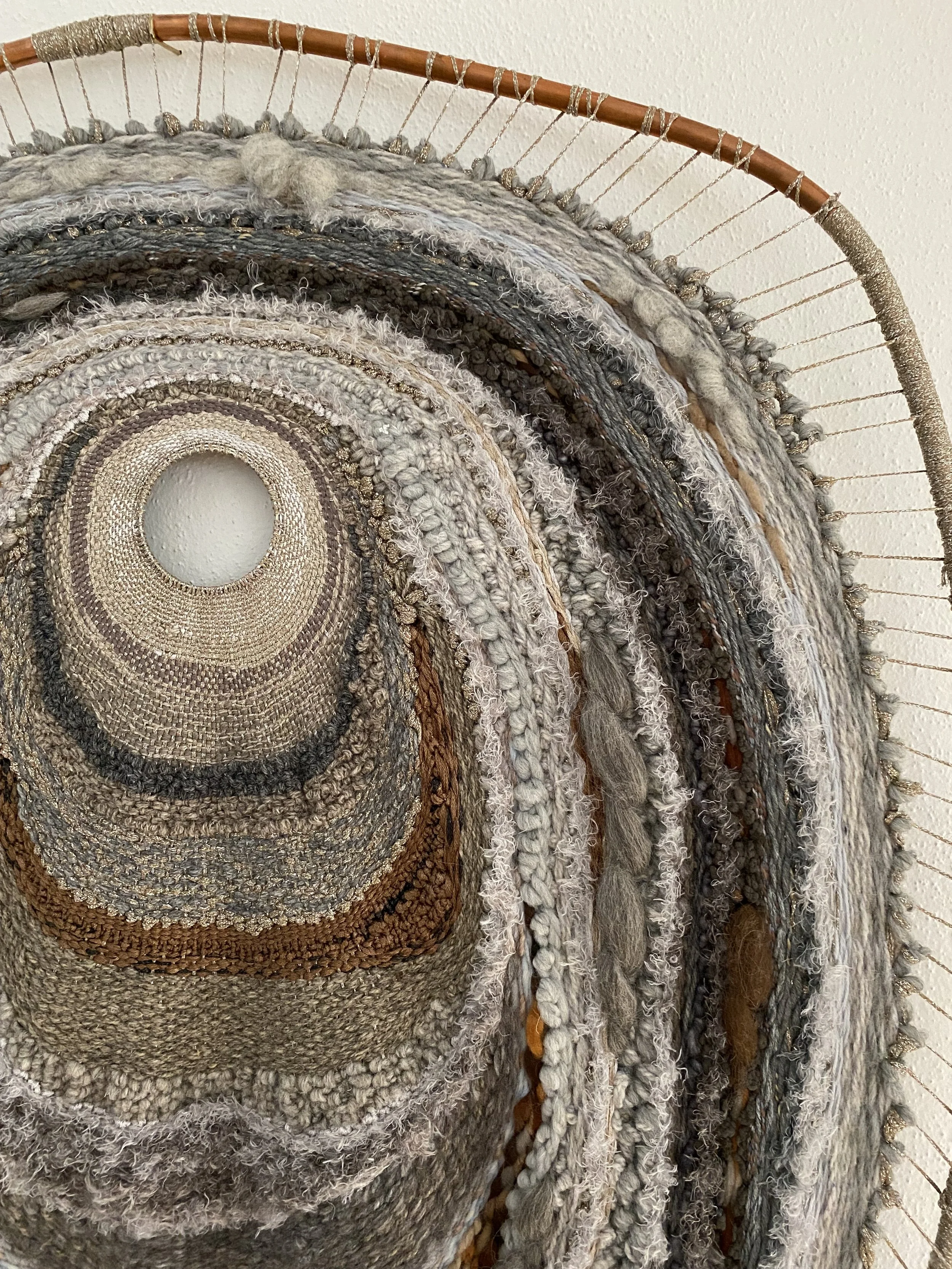 A circular tapestry made from various textured and colored yarns, mounted on a wooden embroidery hoop.