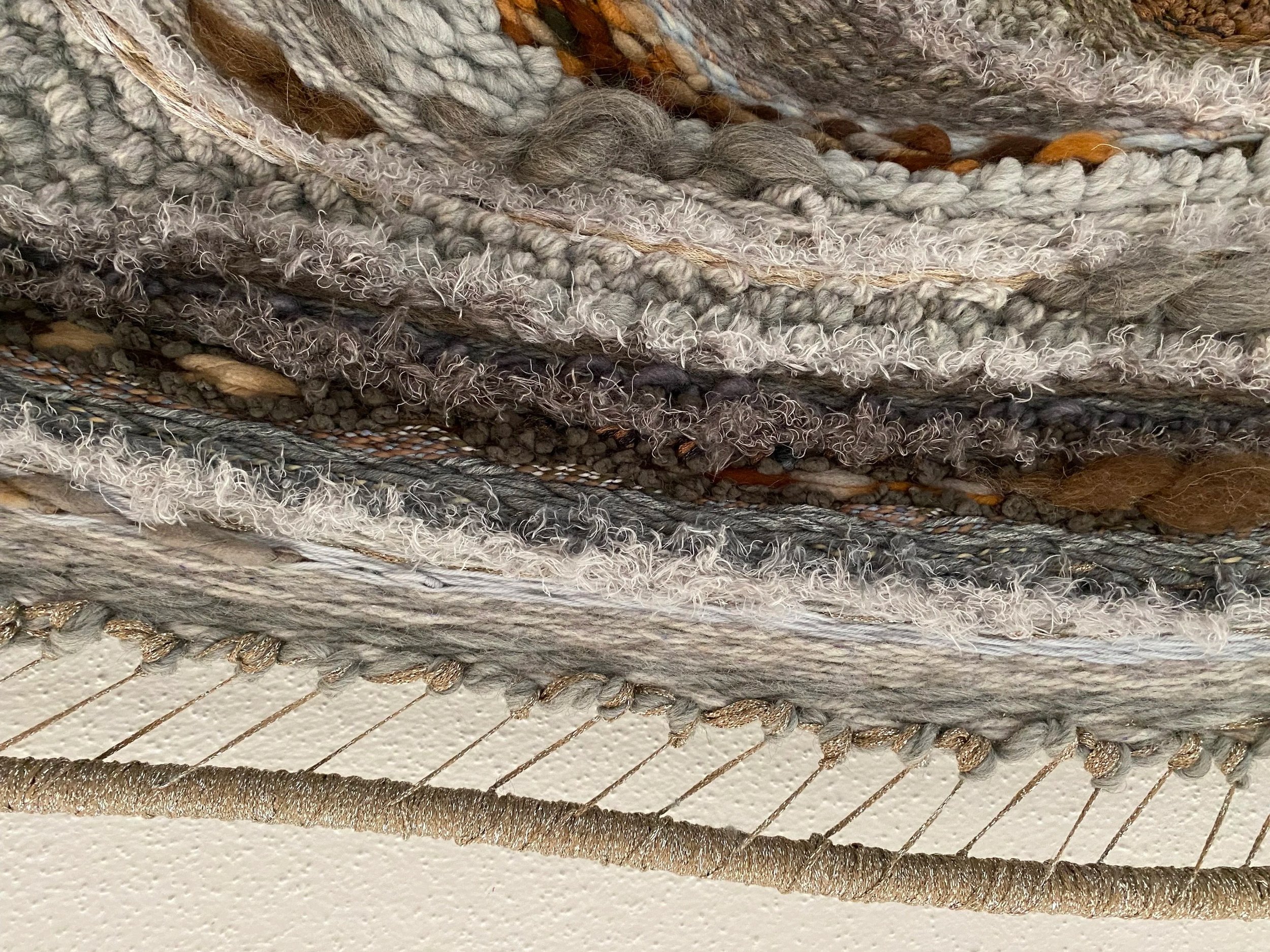 Close-up of a woven textile with various textures and fibers, framed against a white textured background.