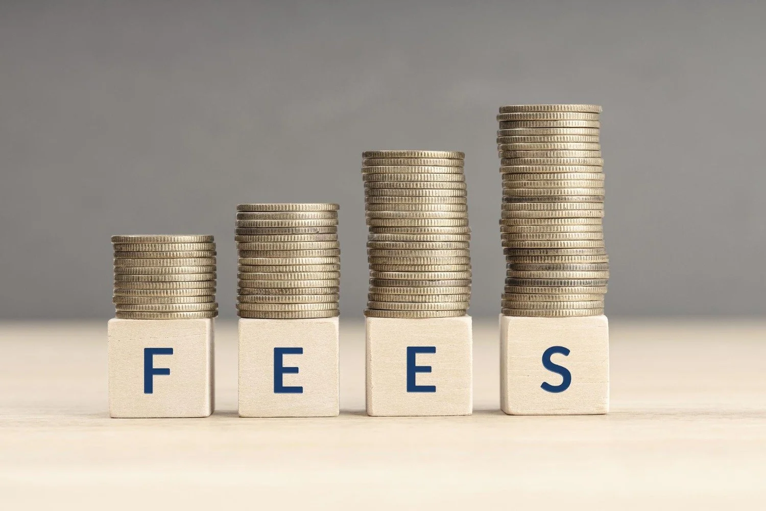 Stacks of coins on wooden blocks spelling 'FEES' against a neutral background.