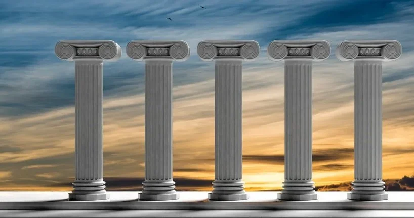 Five ancient Greek or Roman columns stand against a sunset sky.