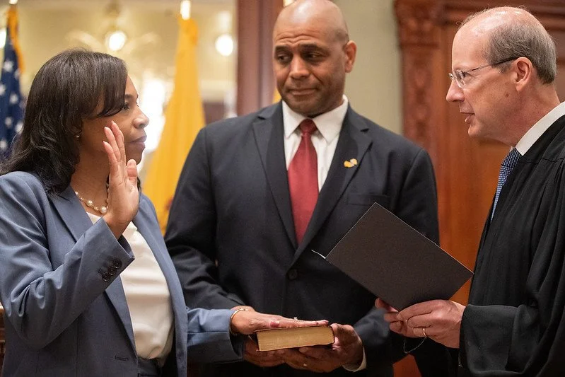Tahesha Way, a woman in a blue blazer is being sworn in as Lieutenant Governor by a judge, while her husband Charles Way in a suit stands nearby watching.