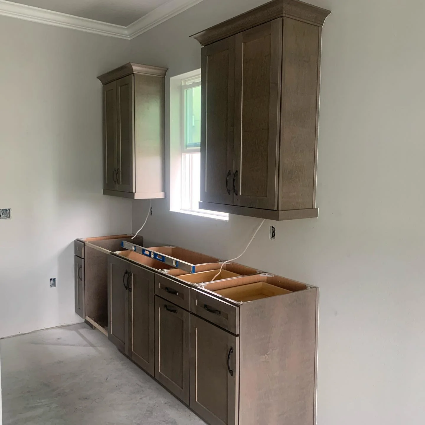Kitchen cabinets under construction with upper and lower wooden cabinets, a small window, and unfinished countertops.