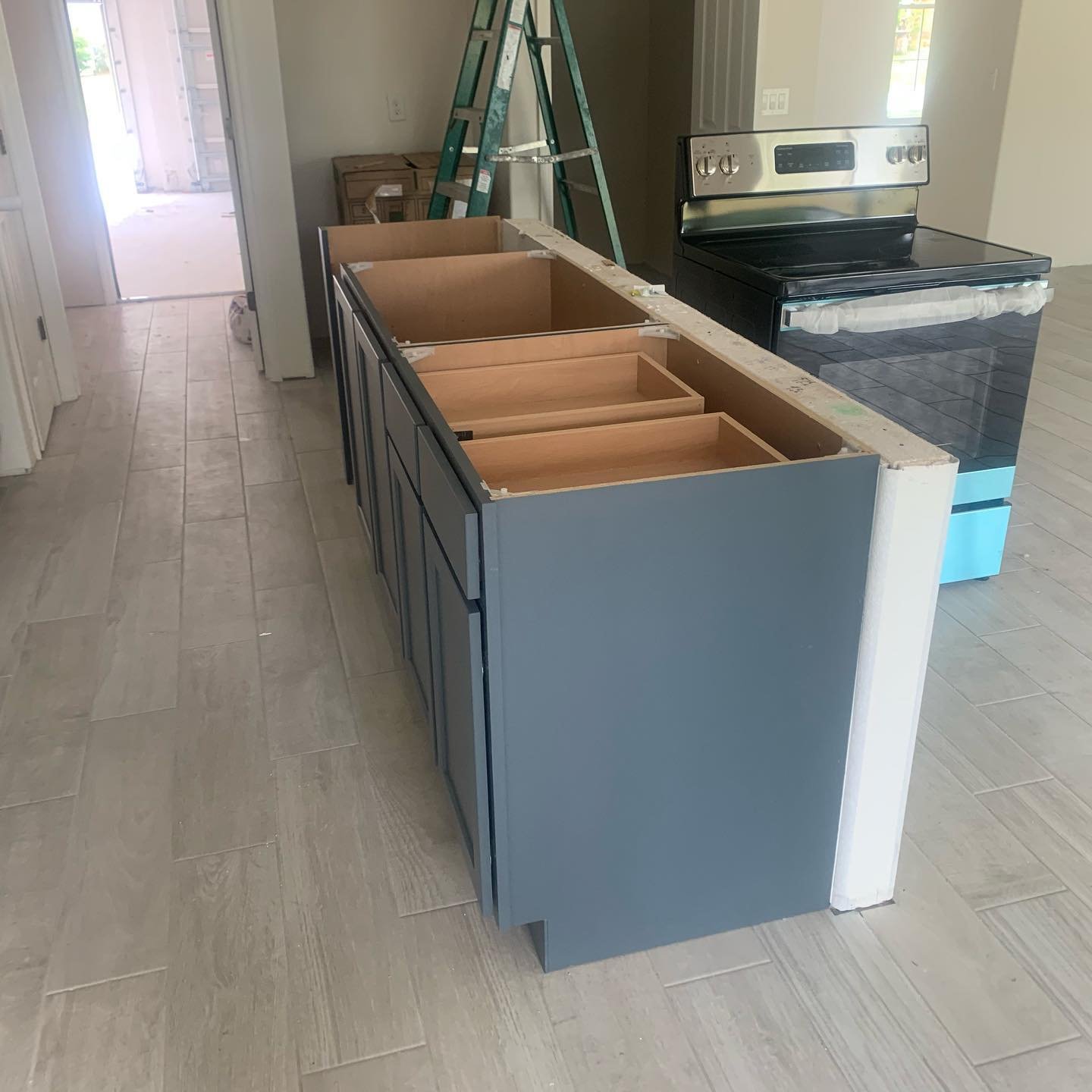Kitchen under renovation with a blue cabinet base, a black stove, and a ladder in the background.