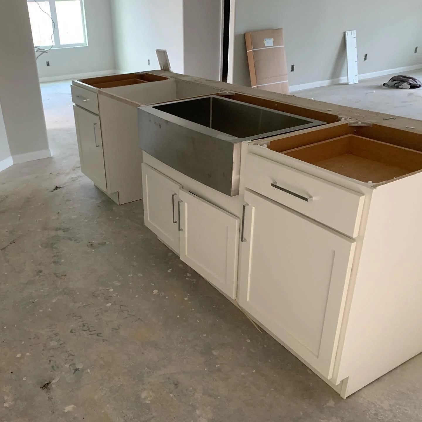 Kitchen island under construction with a white cabinet base, missing countertops and a stainless steel panel, in a room with unfinished flooring.