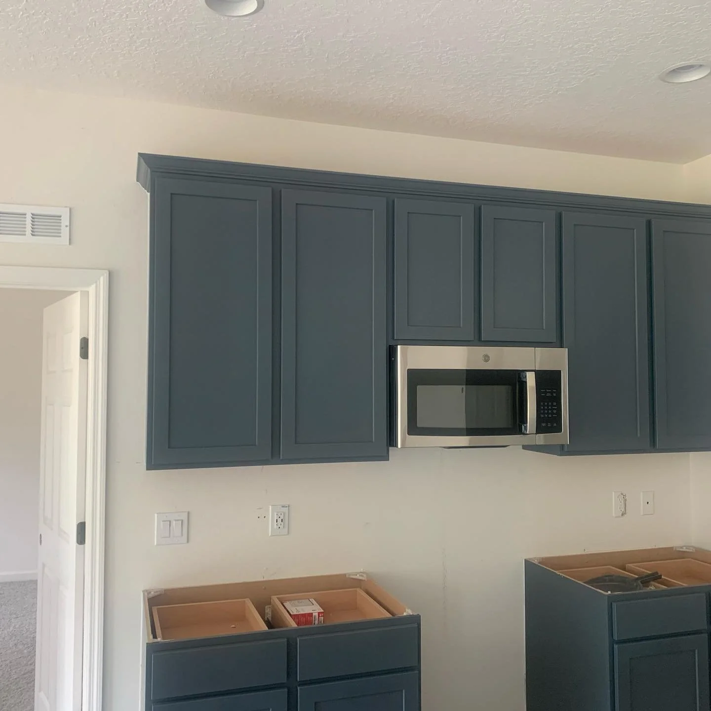 Kitchen with blue cabinets, stainless steel microwave, and some cabinetry still under construction.