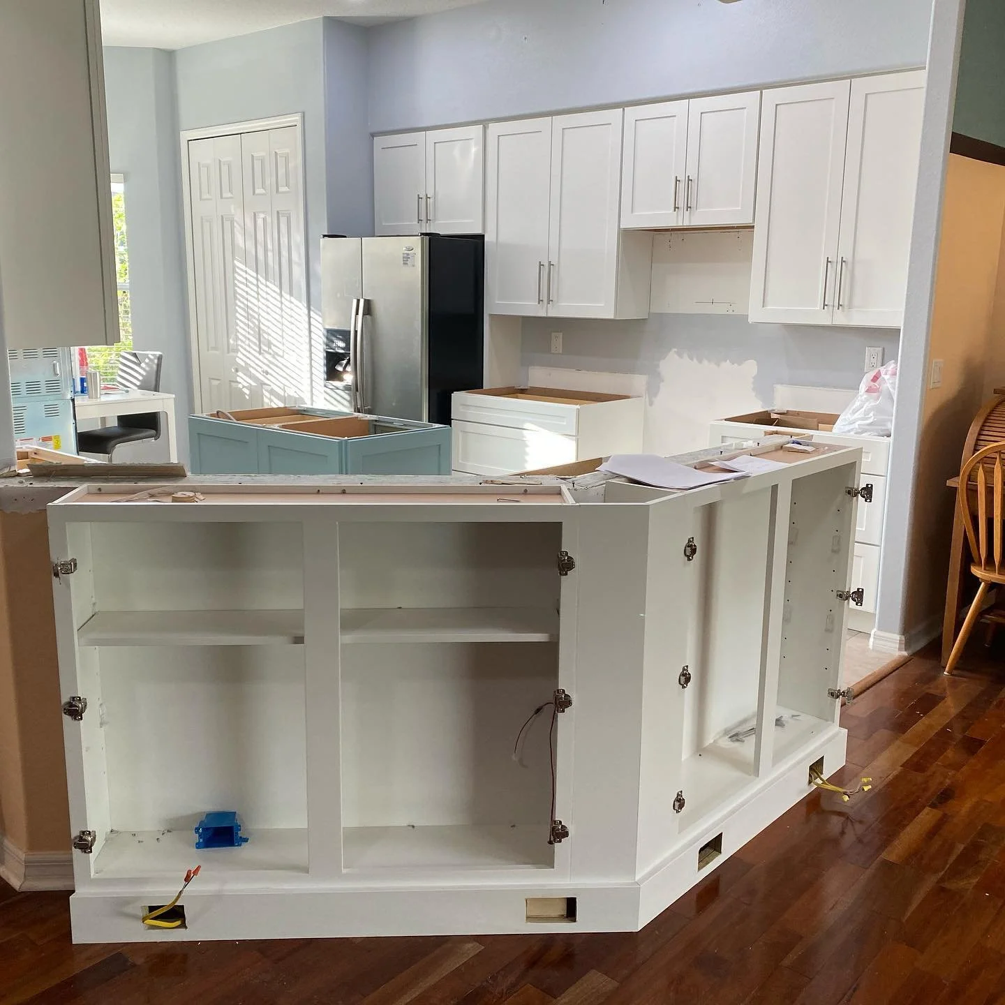 Kitchen under renovation with white cabinets, a silver refrigerator, and an unfinished kitchen island with open cabinets and construction materials on the counter.