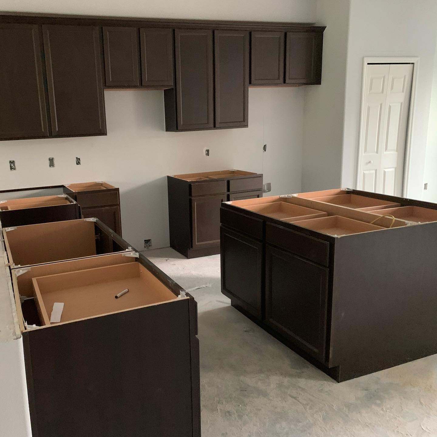 Kitchen under renovation with dark brown cabinets, some installed and others waiting to be installed, and an unused white door.