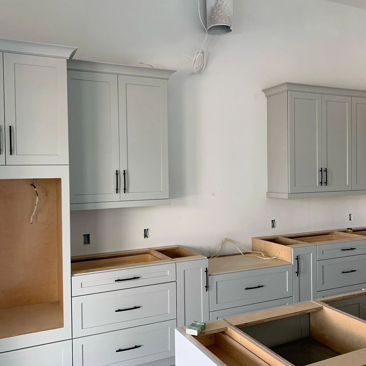 Kitchen with white cabinets, some with black handles, under construction with open drawers and no countertops installed yet.