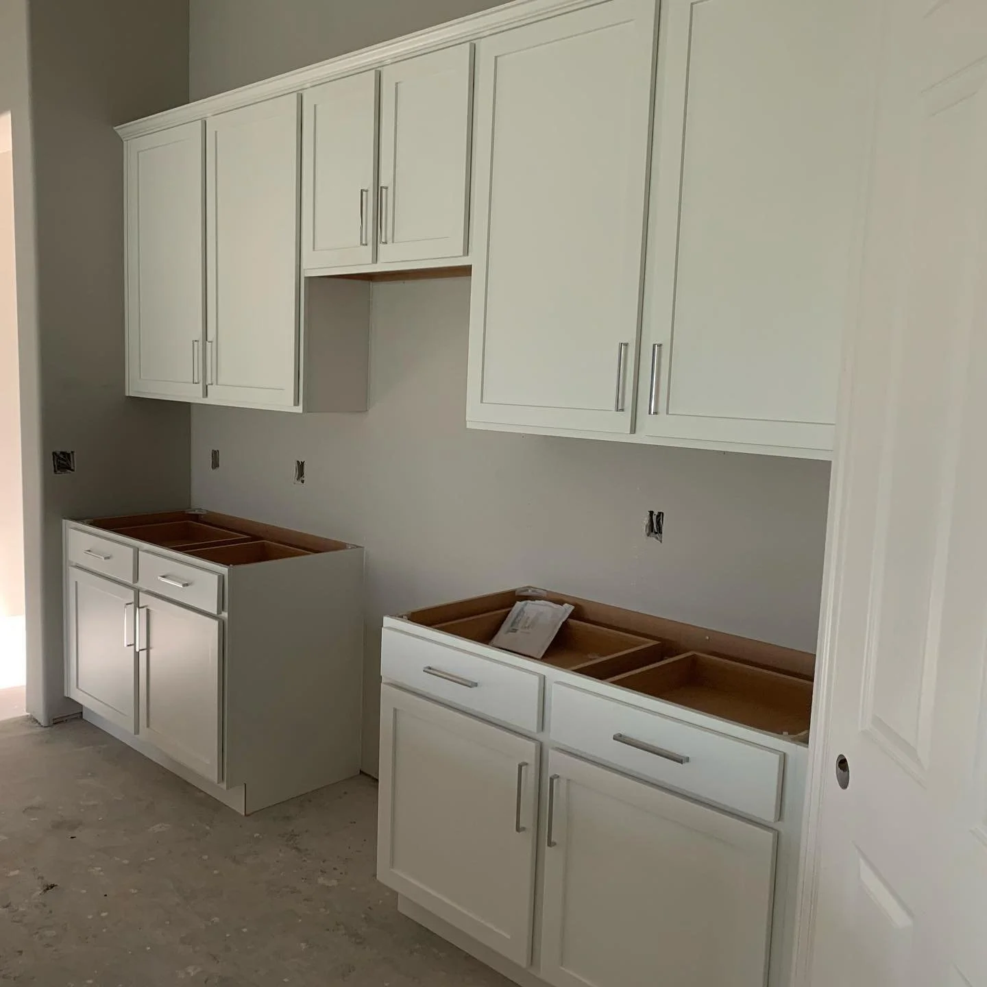 Kitchen cabinets being installed in a new kitchen, with upper and lower white cabinets and no countertops yet.