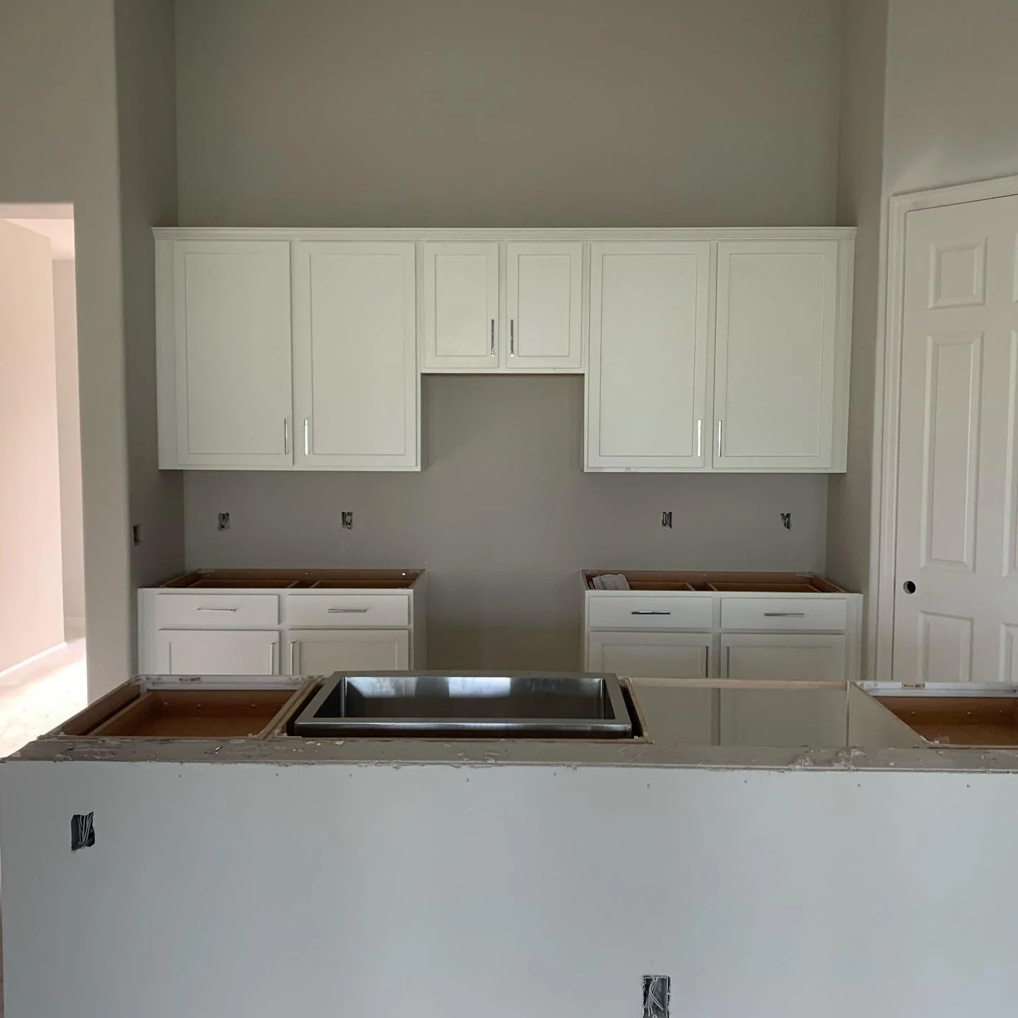 Kitchen under renovation with white cabinets and a countertop with a cutout for a stove or sink.