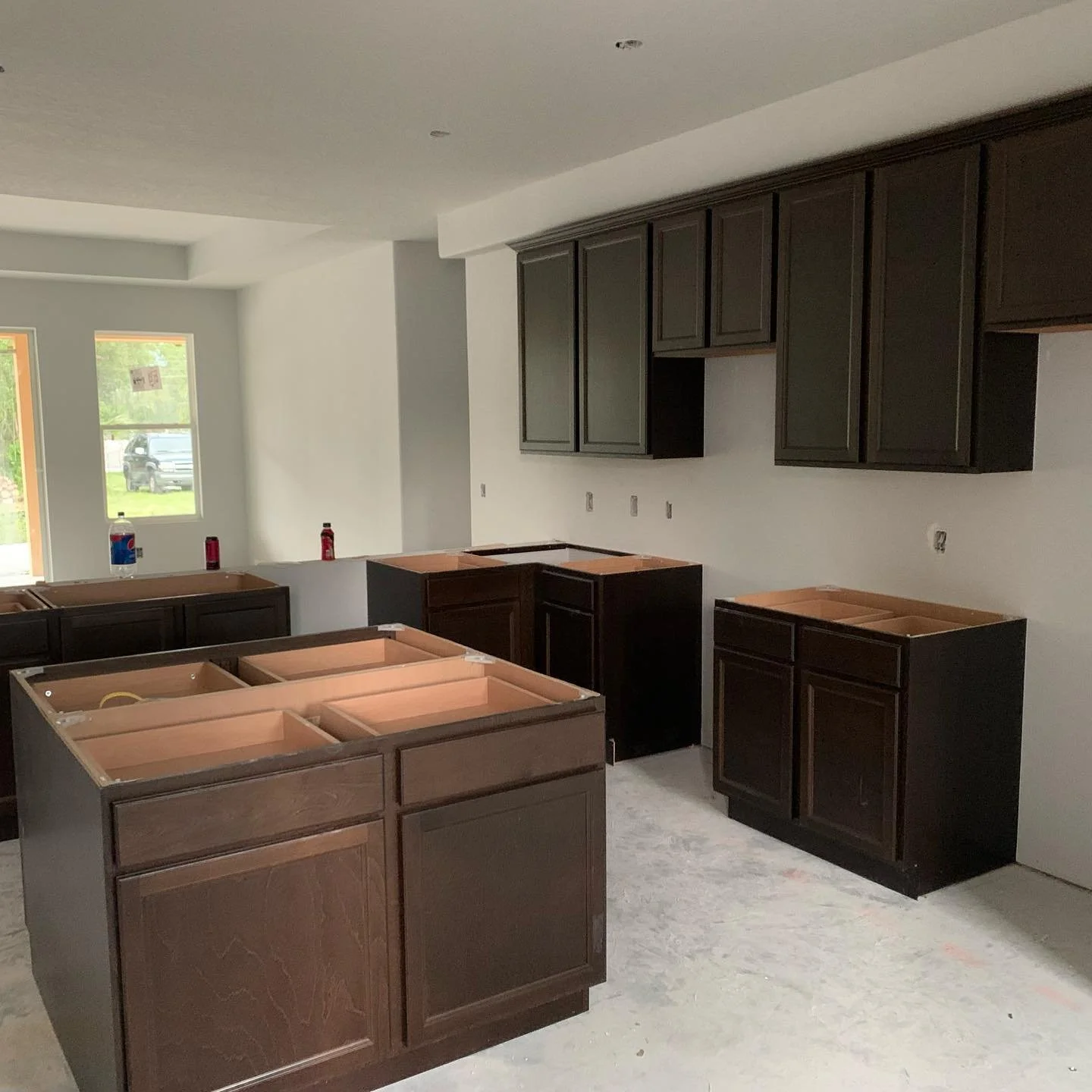 Kitchen under construction with dark wooden cabinets and empty spaces for appliances. Some bottles are on the counters.