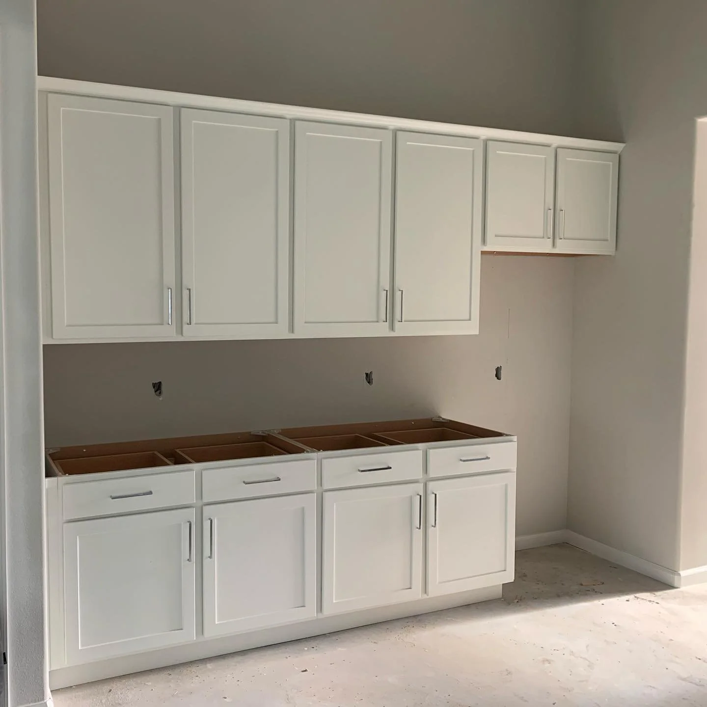 Kitchen cabinets being installed with upper cabinets mounted and lower cabinets without countertops, in an unfinished room.