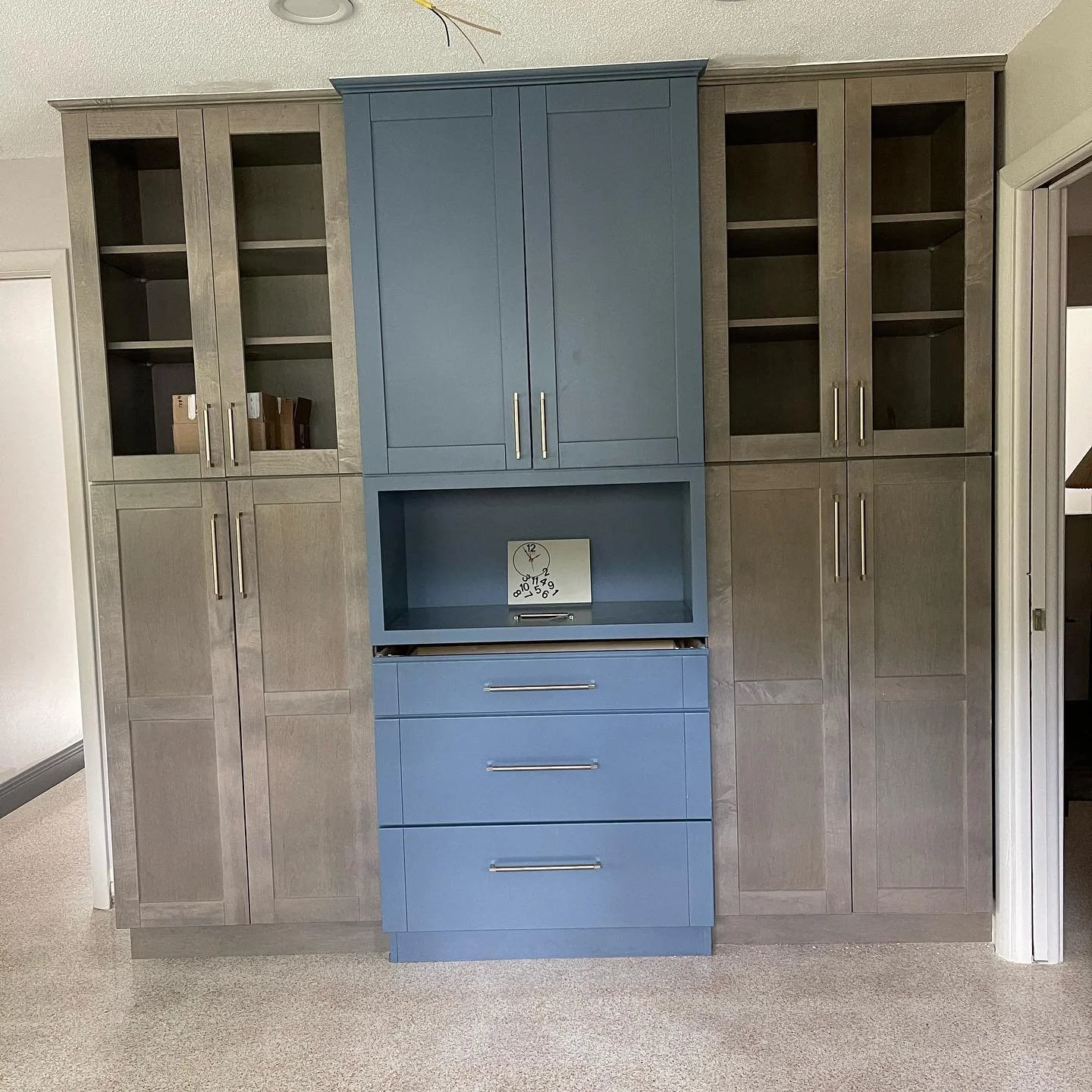 A large built-in cabinet with a combination of open shelves and closed doors, painted in gray and blue, with a small clock placed in an open cubby.