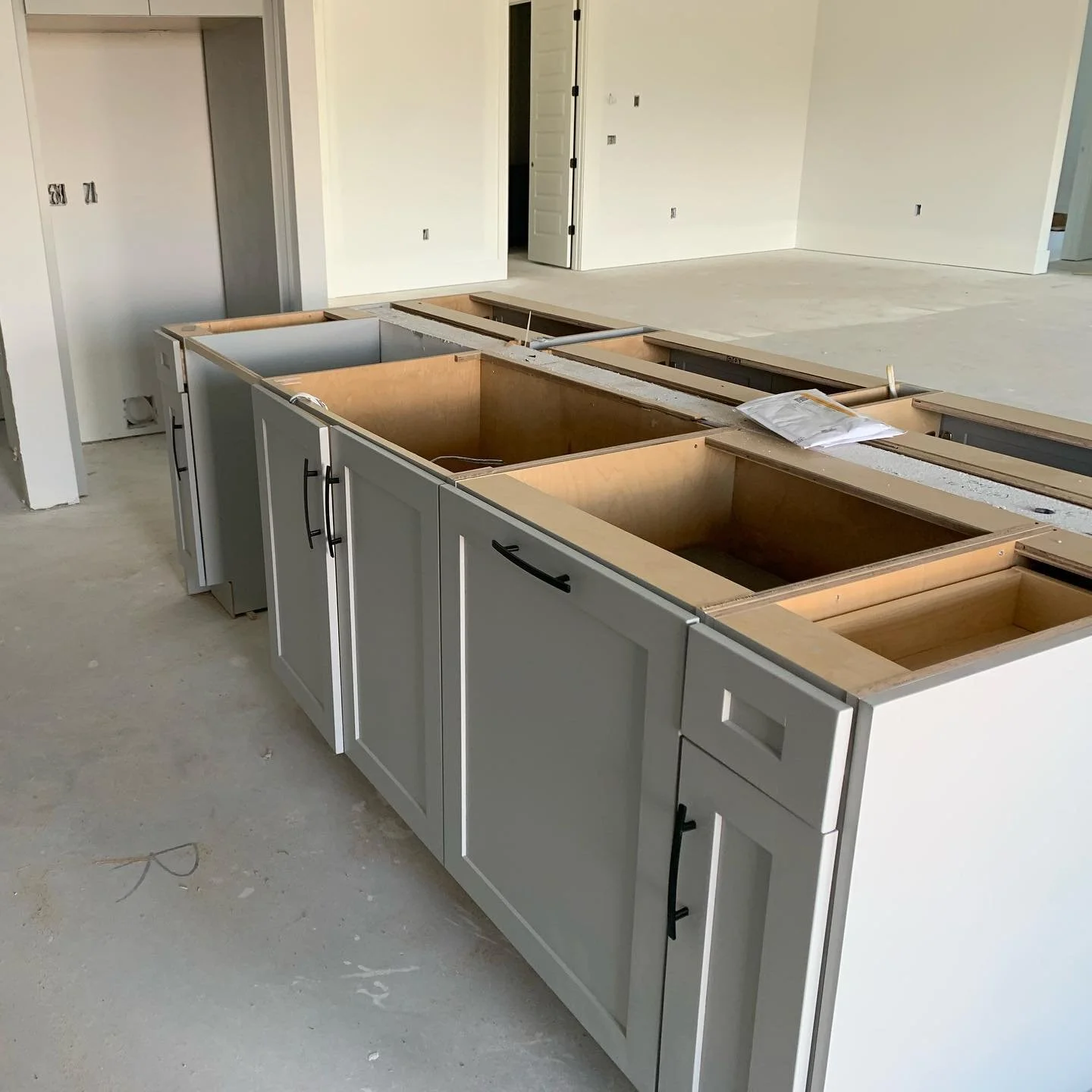 Kitchen cabinets under construction inside a house, with visible white doors and open space in the background.
