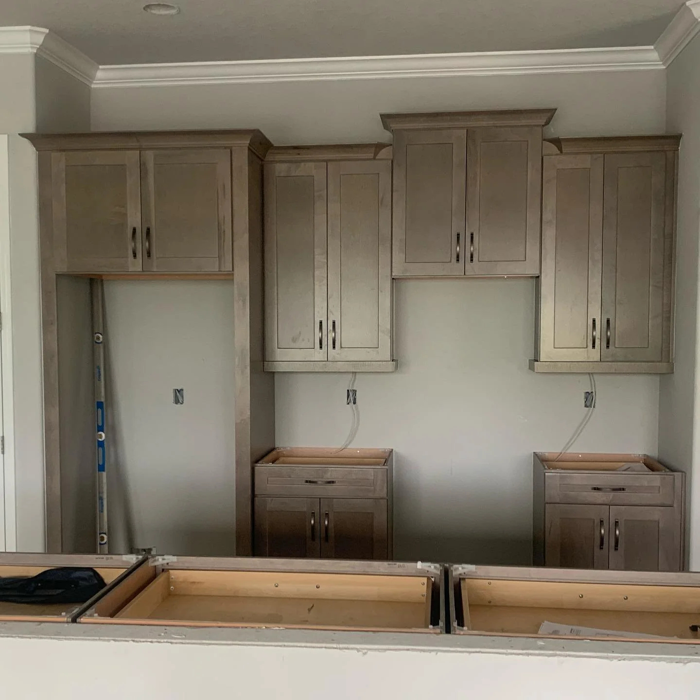 Kitchen cabinets installed with some wires and gaps for appliances, under construction or renovation.