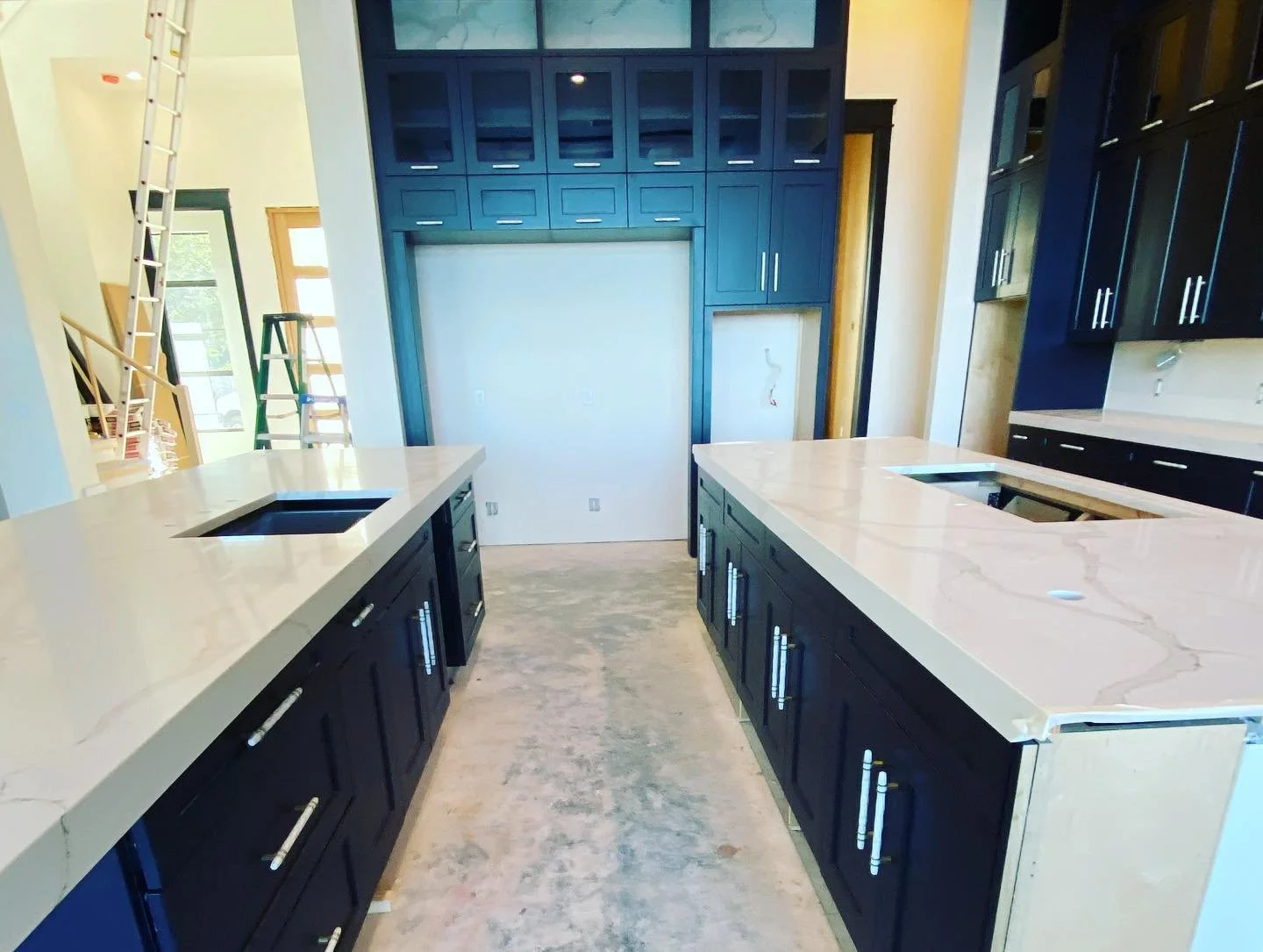 Unfinished kitchen with dark blue cabinets, white marble countertops, and two kitchen islands with built-in sinks, during construction or renovation.