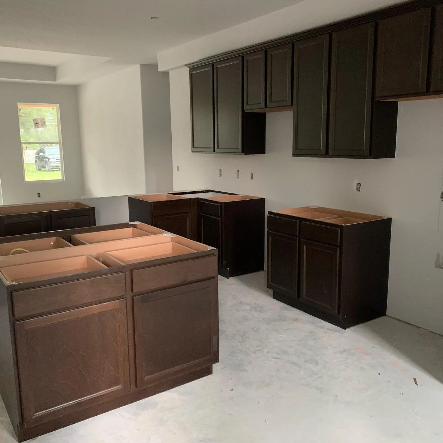 Kitchen under construction with dark wood cabinets, no countertops installed, and empty space for appliances.