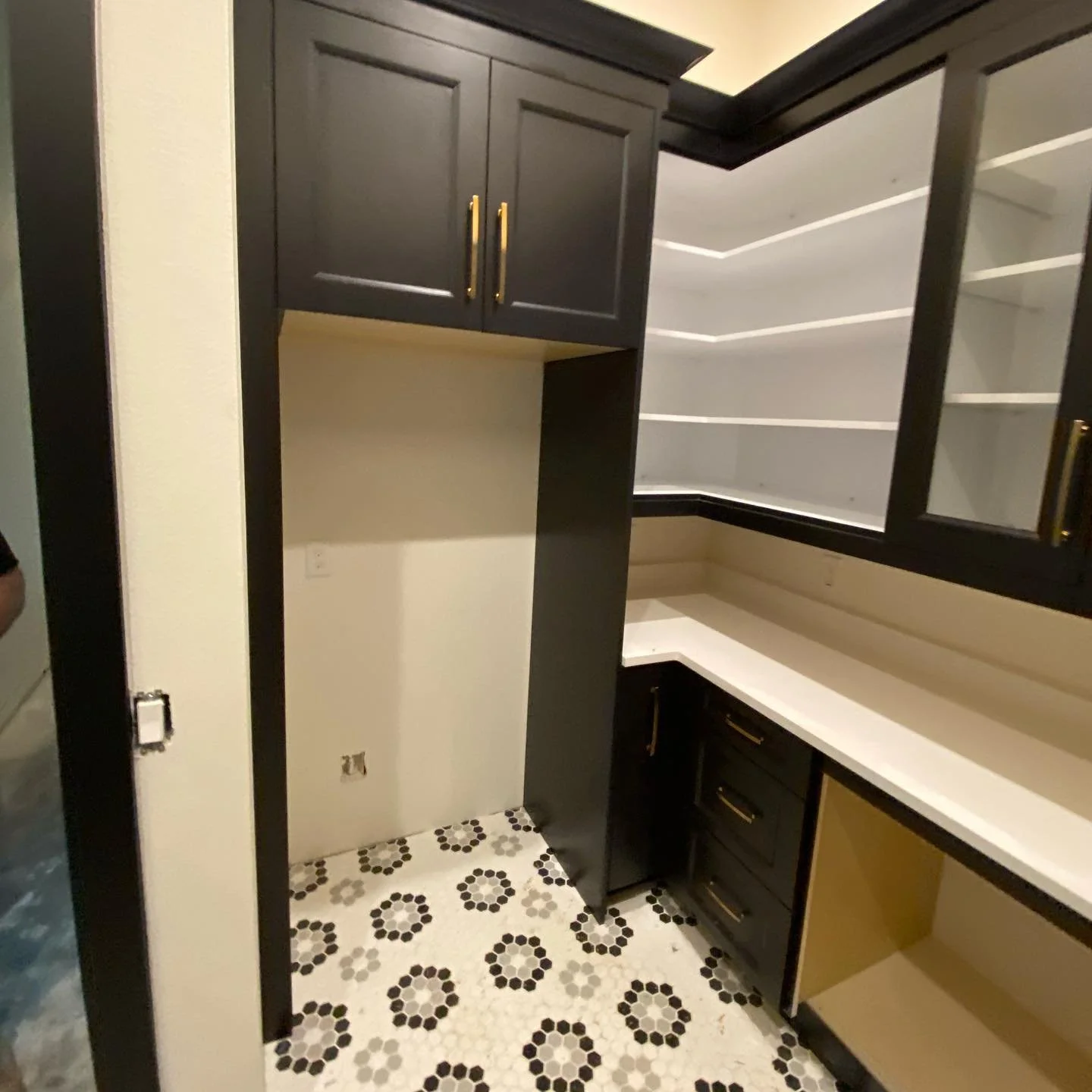 Interior of a kitchen undergoing renovation, showing black cabinets, white countertops, and patterned black and white floor tiles.