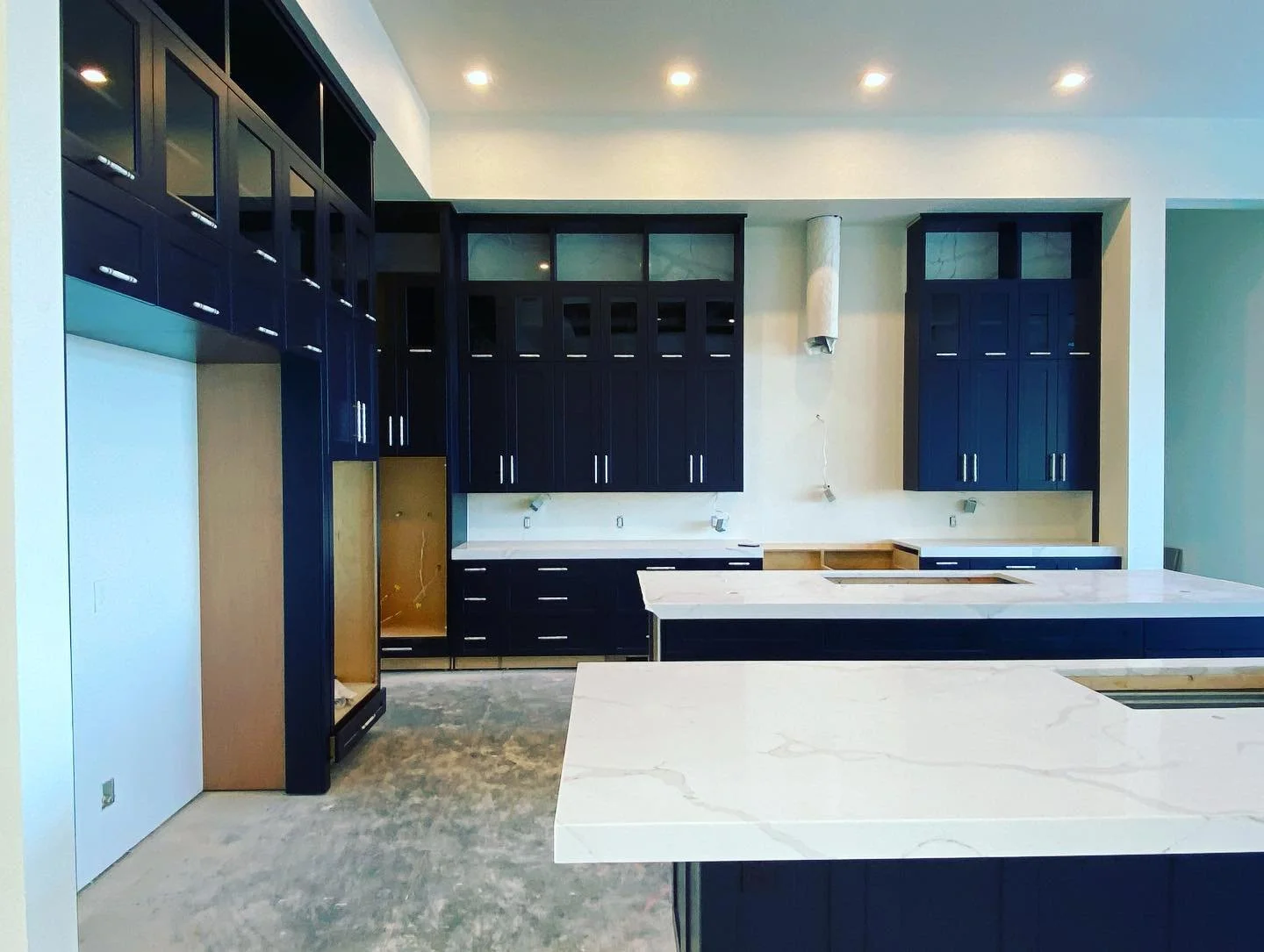 Modern kitchen under construction with dark blue cabinets, white marble countertops, and unfinished flooring.