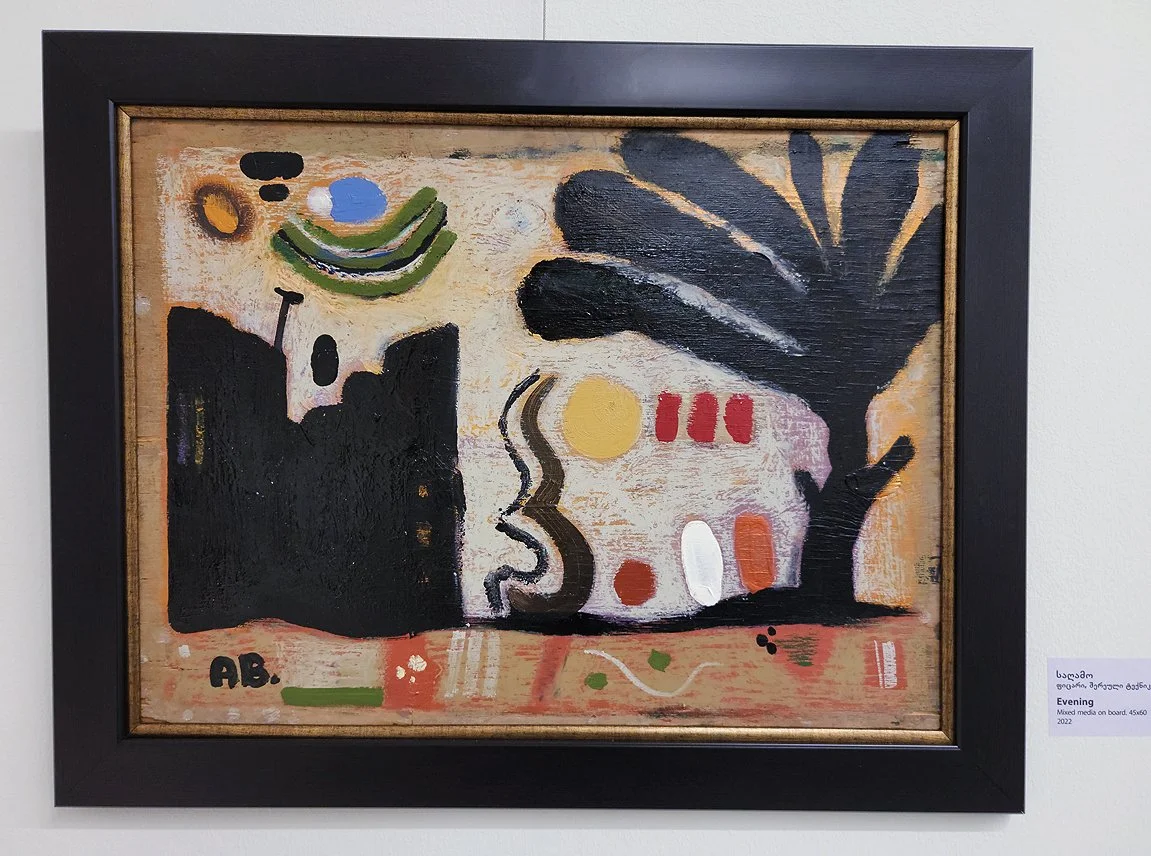 Abstract painting with black, green, red, yellow, white, and pink shapes and lines, featuring a black tree silhouette on the right, a black building silhouette on the left, and a yellow circle resembling the sun or moon.