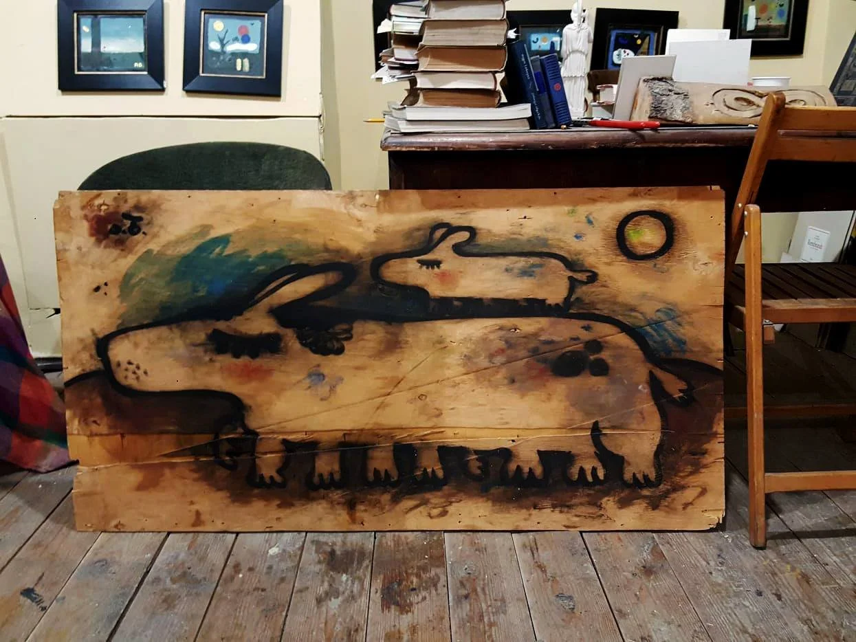 Wooden art piece with abstract black outline of a animal, possibly a dog or wolf, on a natural wood background, placed on a wooden floor in an indoor room.