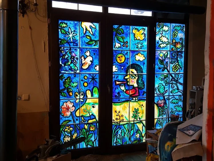 Colorful stained glass window with a woman looking through a telescope, surrounded by various nature-themed images including flowers, animals, and celestial objects.