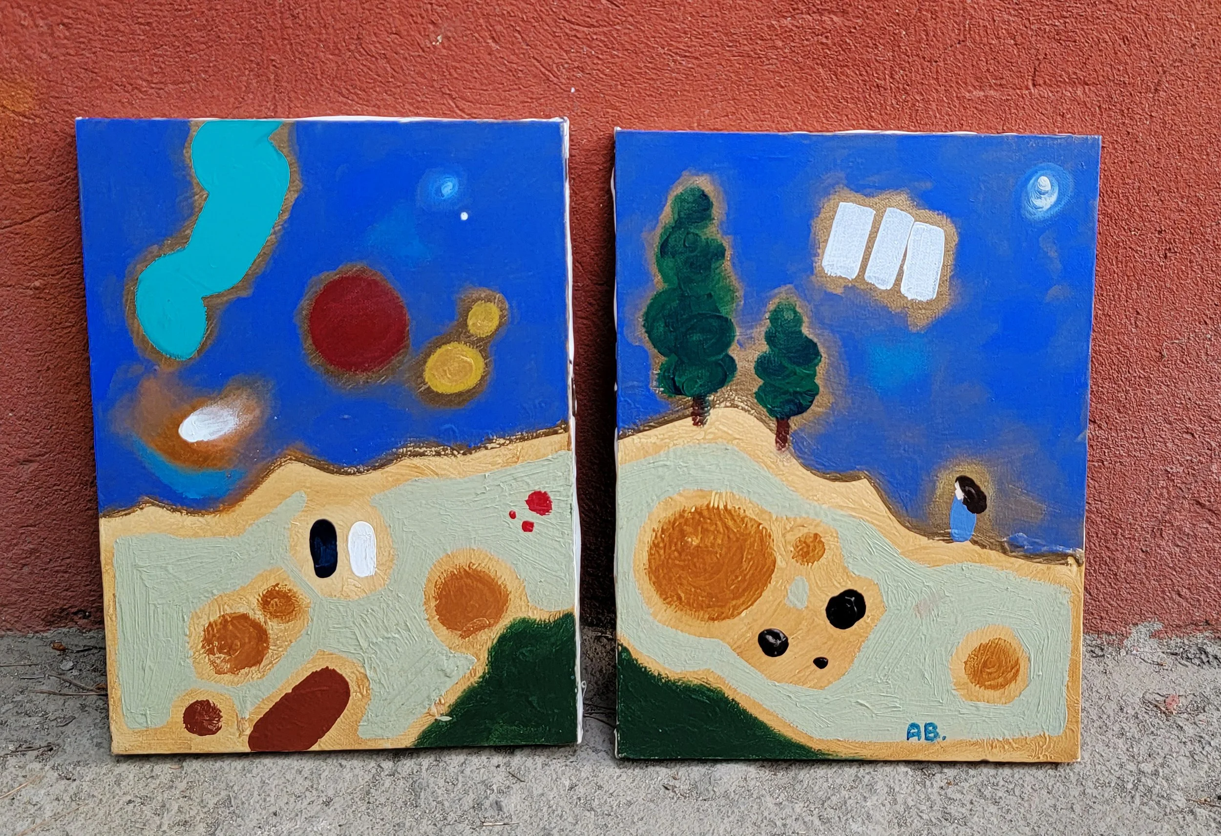 Two colorful abstract landscape paintings with a blue sky, green trees, and various shapes, mounted on a reddish-brown wall.