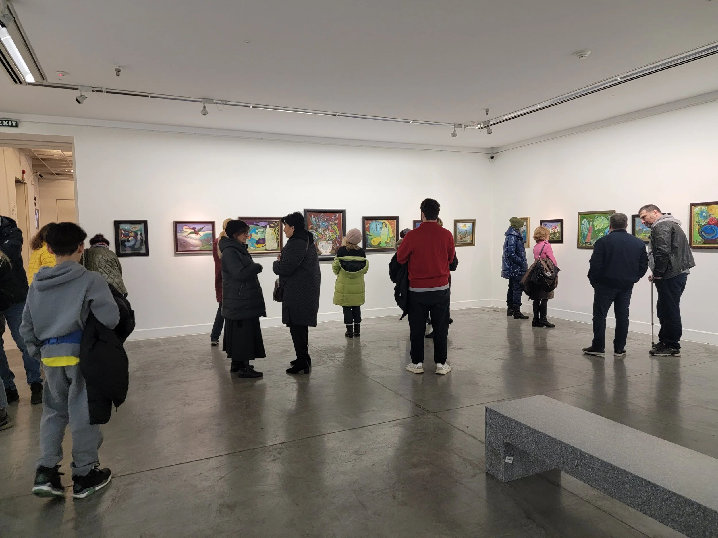 People observing artwork in an art gallery with white walls and gray concrete floor.