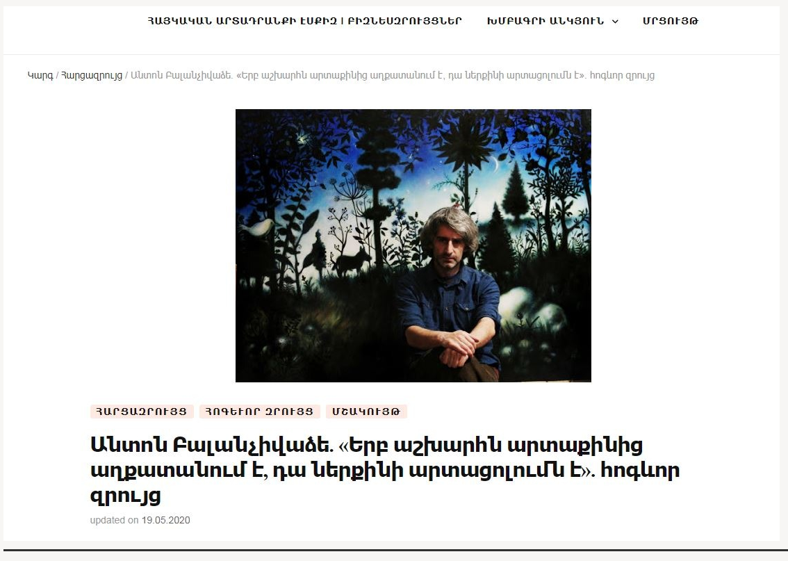 Anton Balanchivadze sitting in front of his painting, painted colorful forest backdrop with trees, animals, and a starry sky.